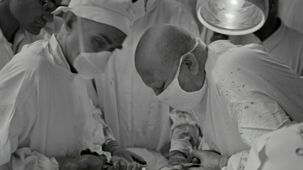 Black and white photo of surgeons working furiously on a patient.