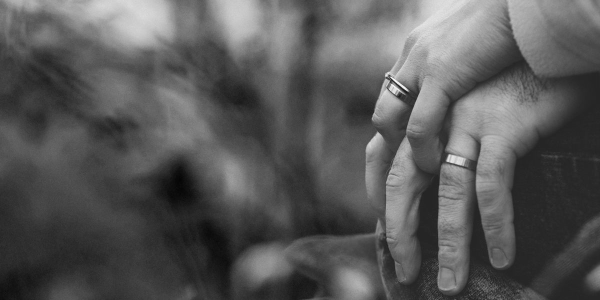 Black and white photo of two people holding hands, their wedding rings showing