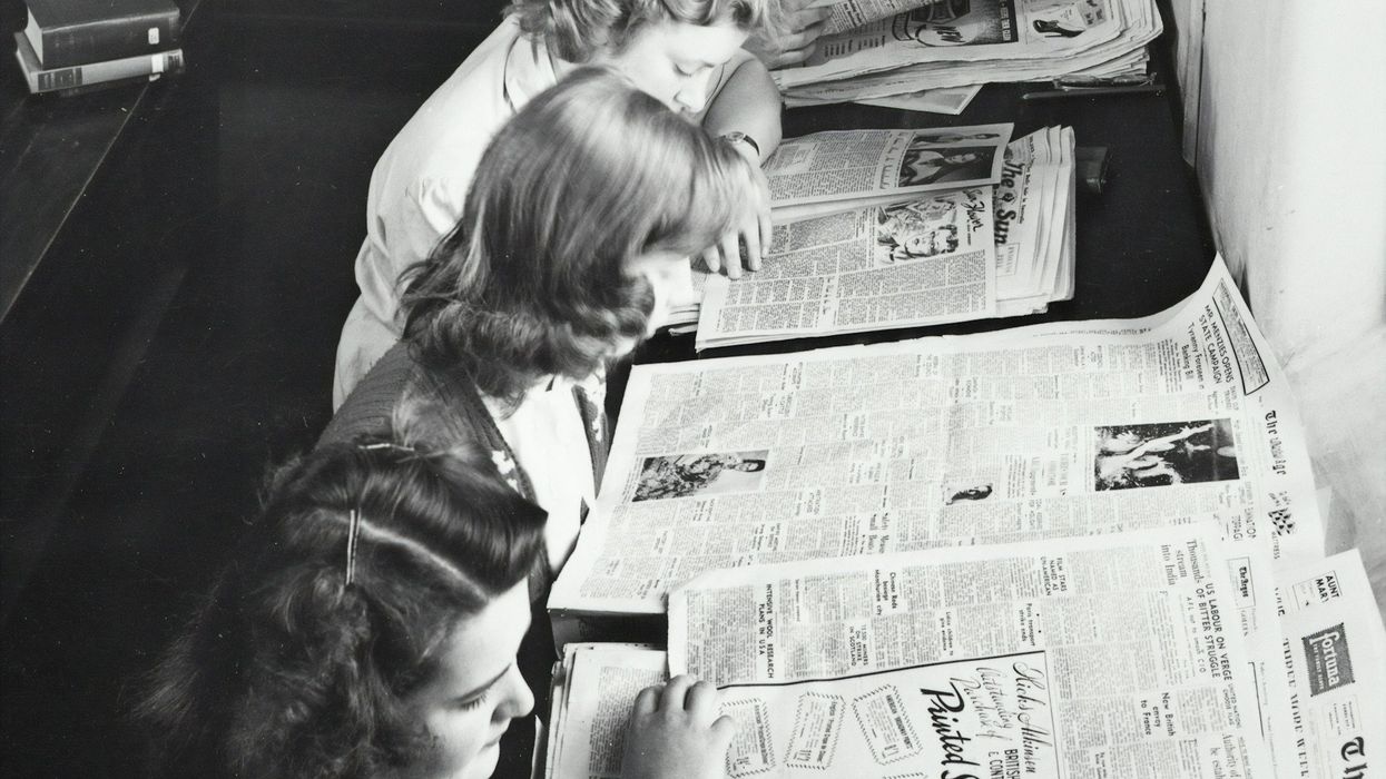 Black and white photo of young women in the 50's pouring over newspaper clippings.