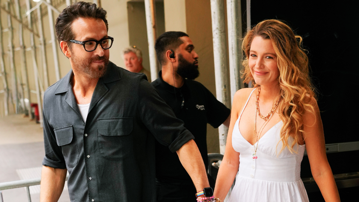 Blake Lively and husband Ryan Reynolds walk out of a venue holding hands and smiling. Lively is looking at the camera, while Reynolds is looking back toward Lively.