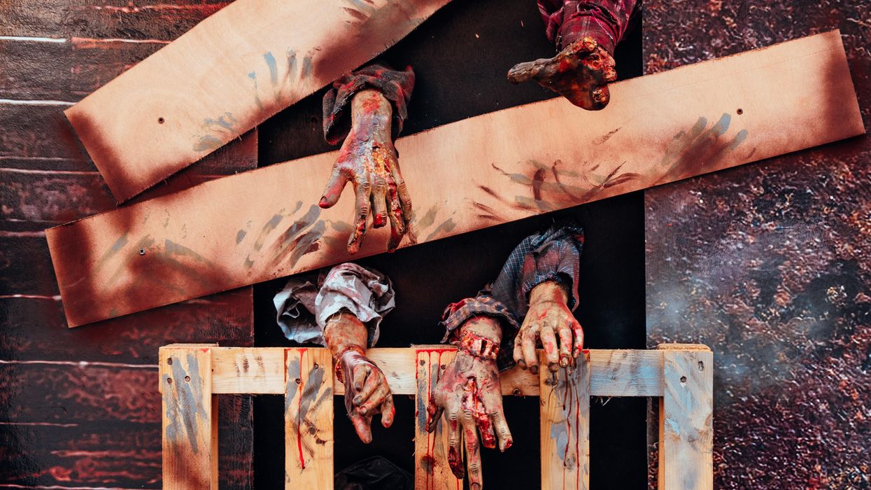 bloodied zombie arms reach out from behind wooden barrier