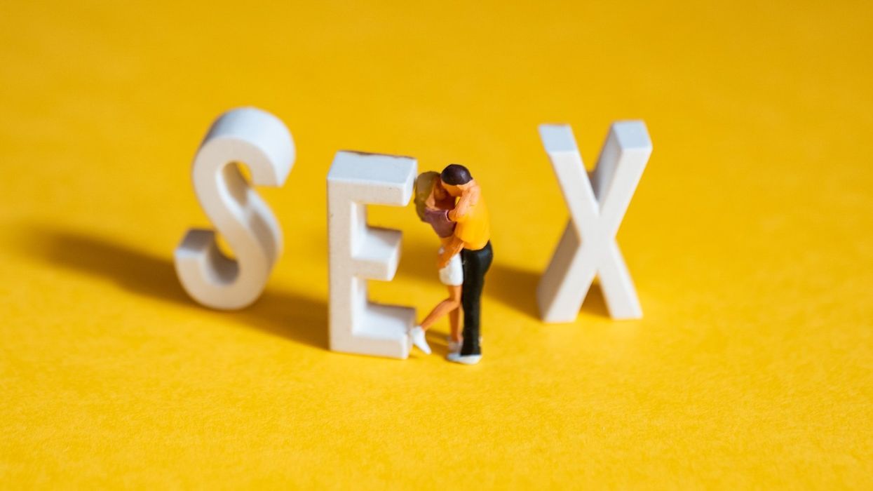 Clay people kiss on a yellow floor, against the letter E in a clay version of the word SEX