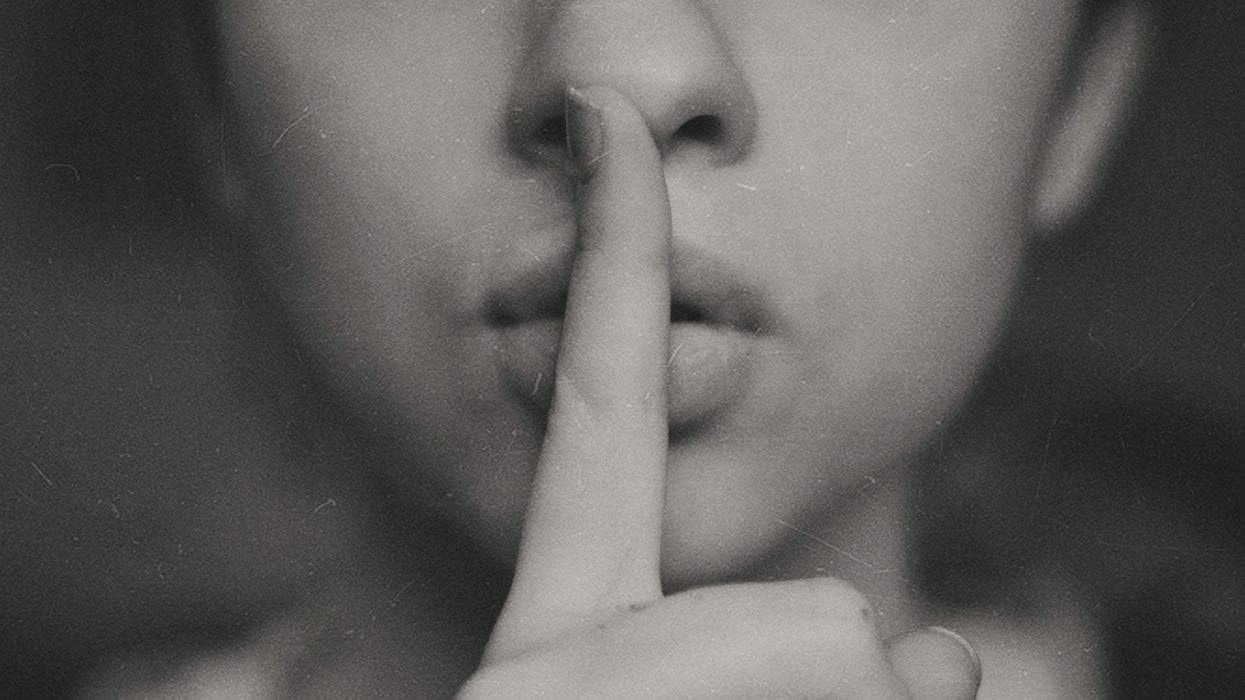 Close-up black and white photo of a young woman placing a finger over her mouth, hushing us.