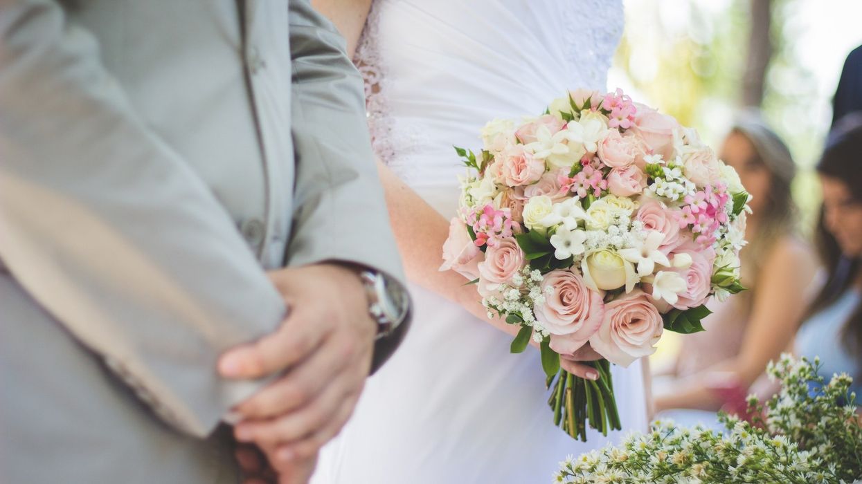 Close up, mid-section shot of a bride and groom at the altar, his hands clasped, her's holding her bouquet
