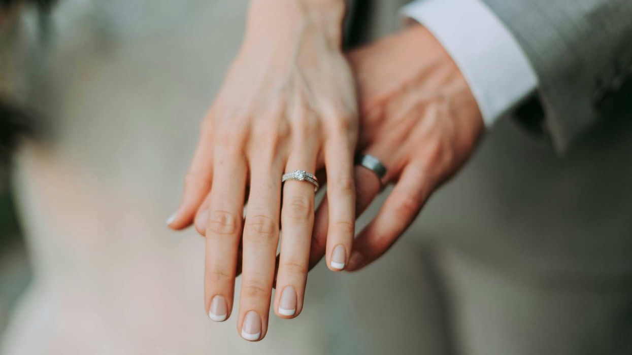 Close-up of a bride and groom's hands, layered, her hand on top of his, emphasizing their rings.