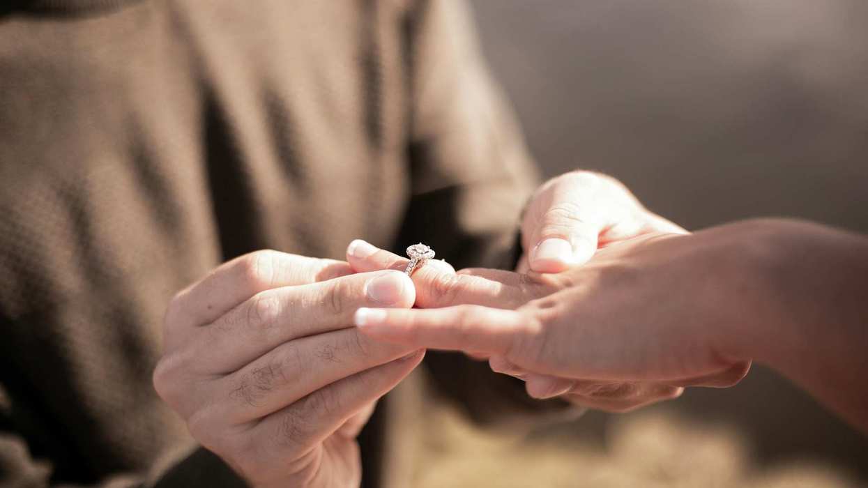 Close-up of a man slipping an engagement ring on a woman's finger.