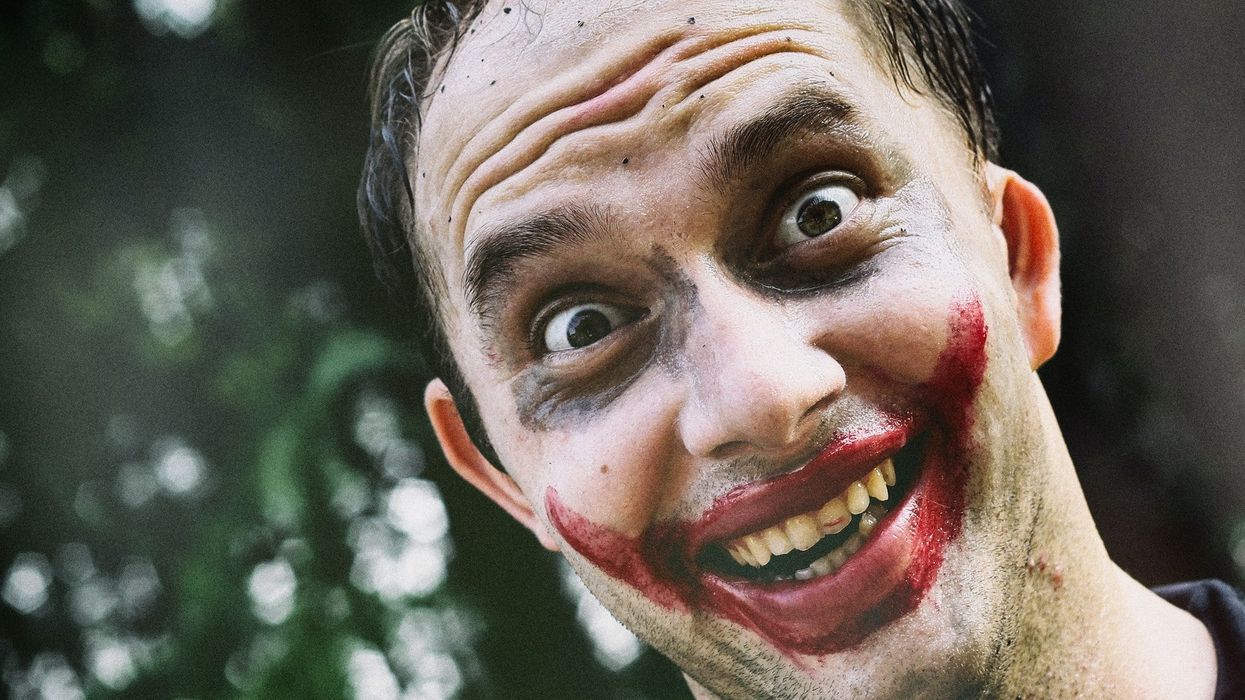 Close-up of a man wildly smiling with his face painted like the joker