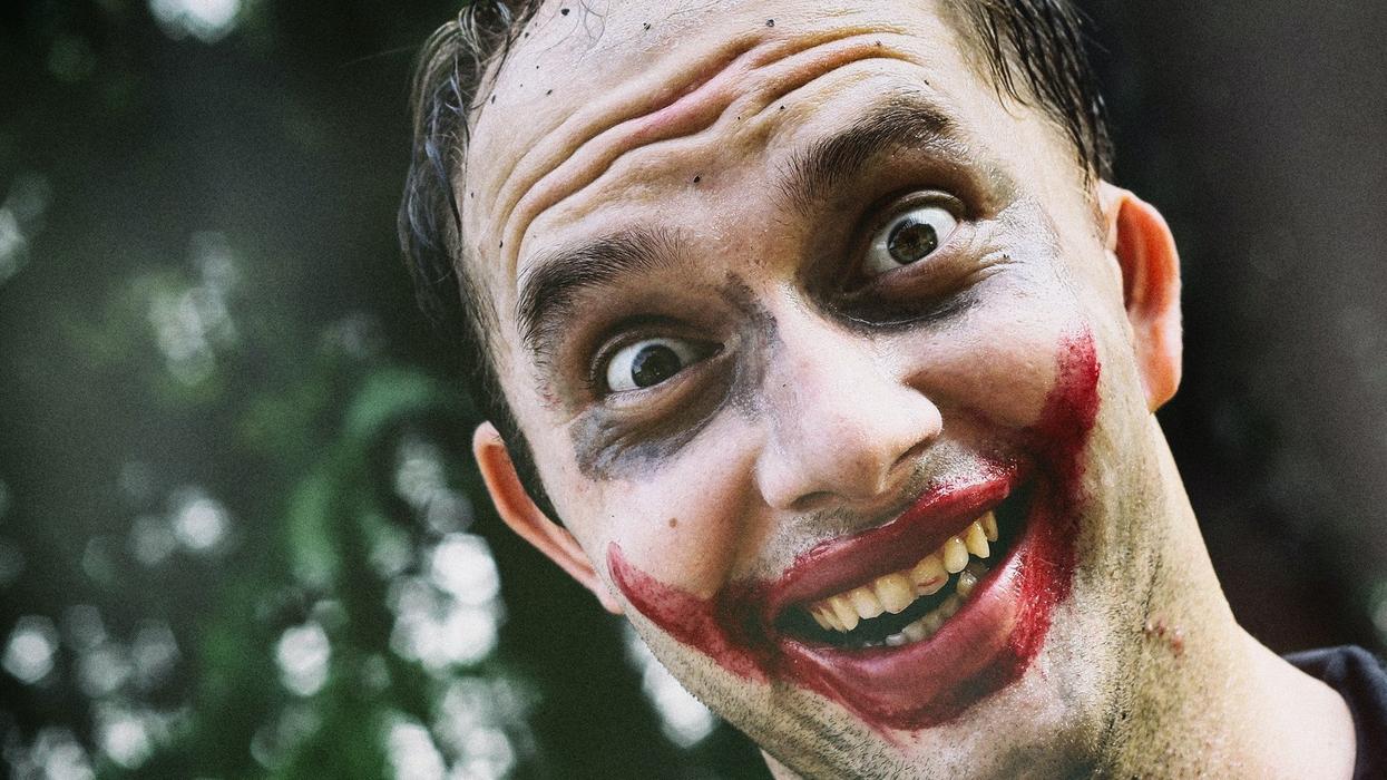 Close-up of a man wildly smiling with his face painted like the joker