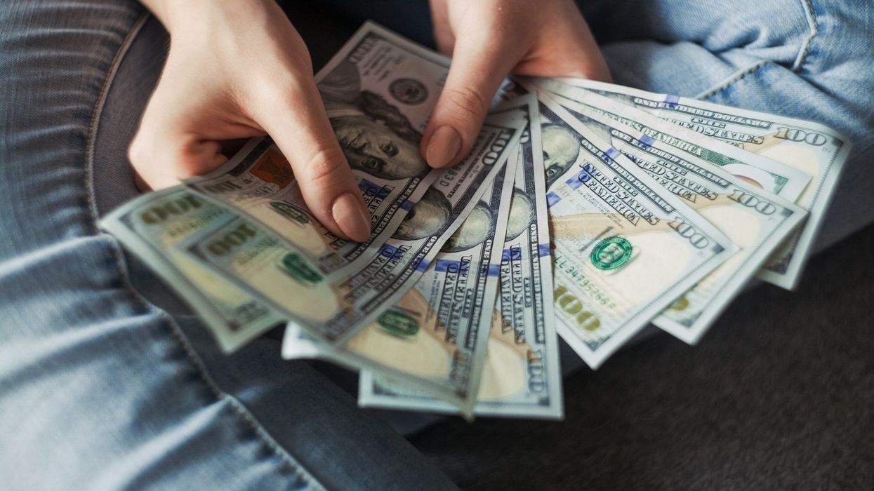Close-up of a woman's hands fanning out hundred dollar bills. She's wearing denim jeans.