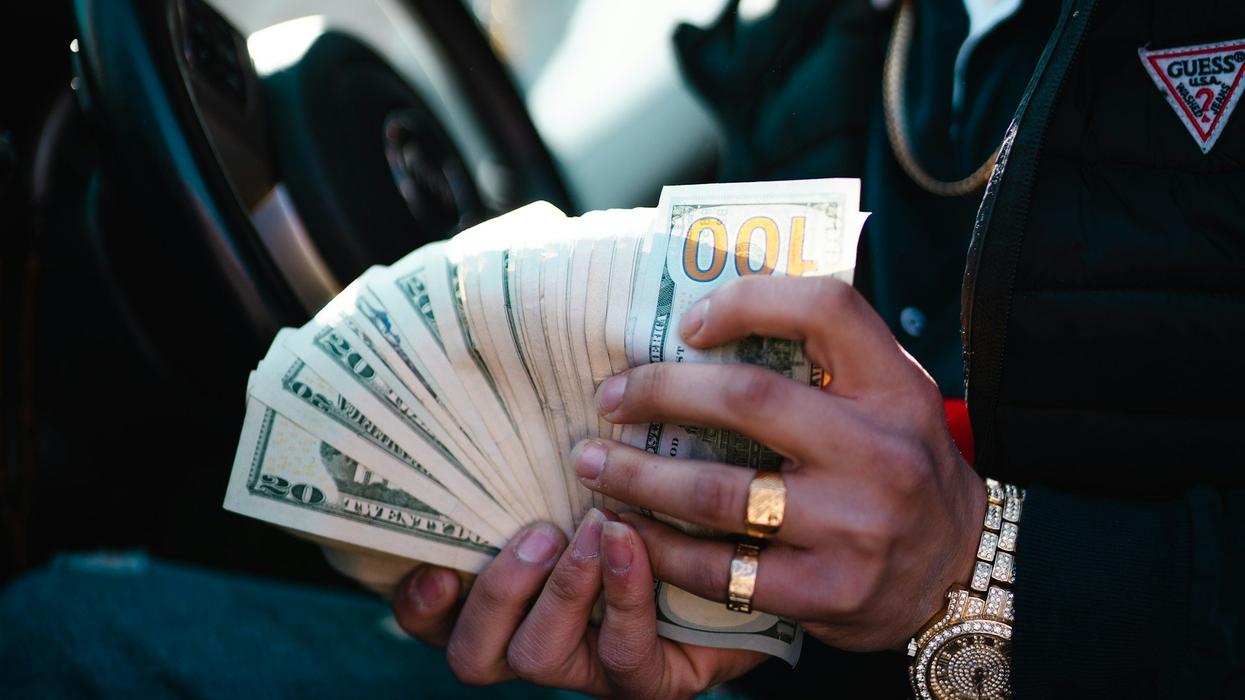 Close up of a young man fanning out hundred dollar bills and twenty dollar bills. He is wearing expensive rings and a watch.