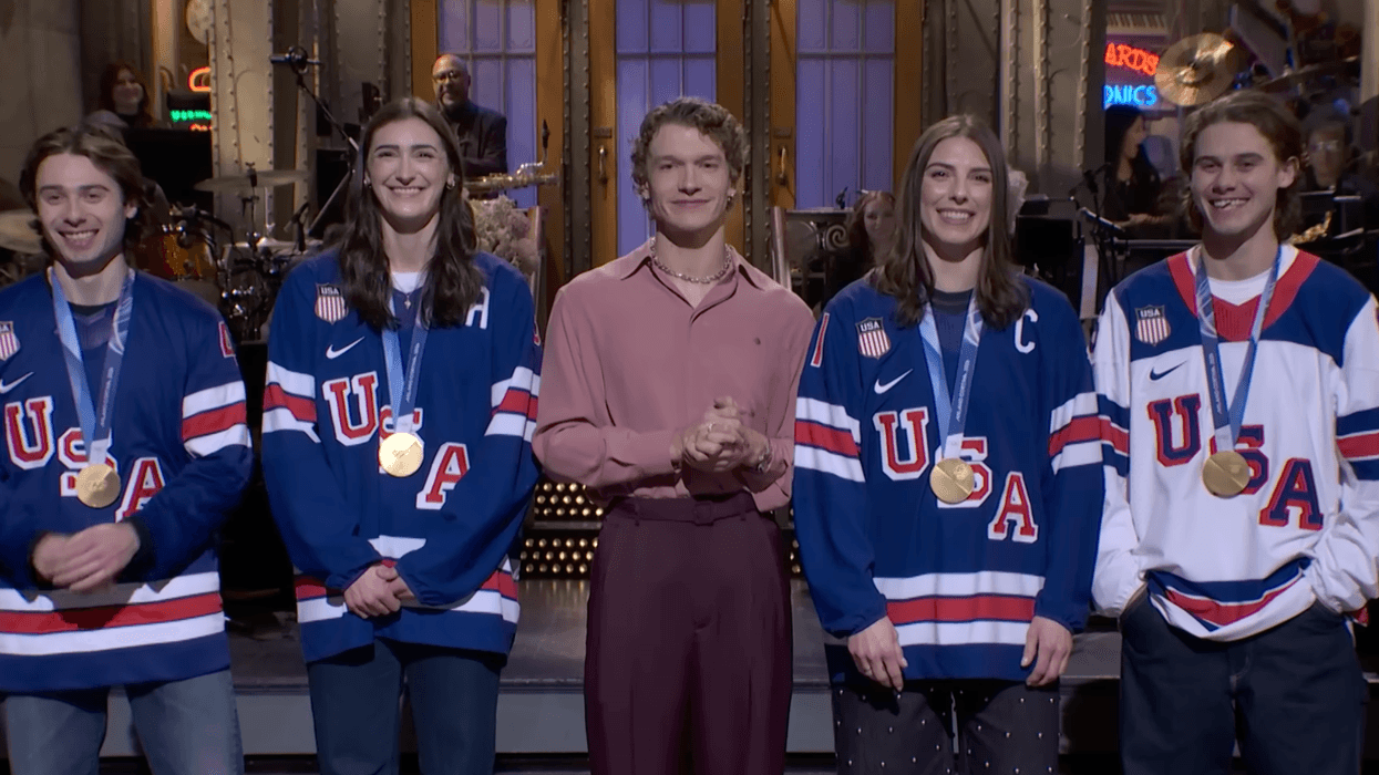 Connor Storrie stands center stage on Saturday Night Live alongside U.S. Olympic gold medalists Quinn Hughes (far left), Hilary Knight (left), Megan Keller (right), and Jack Hughes (far right) during his opening monologue in Studio 8H.