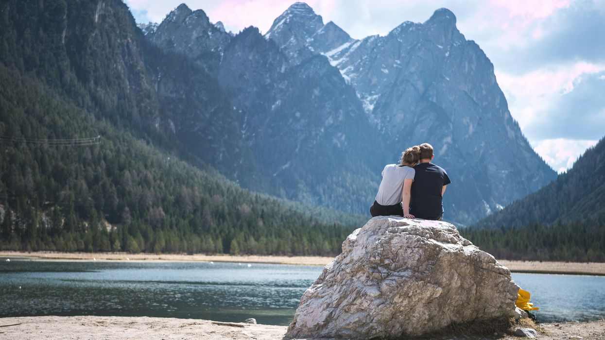 Couple sitting atop a large rock and overlooking a lake
