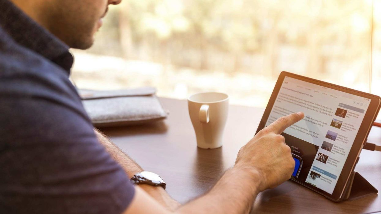 Cropped photo of a man tapping on his IPad while having a cup of coffee.
