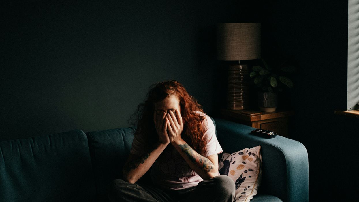 distressed person with head in hands sitting in darkness on black couch