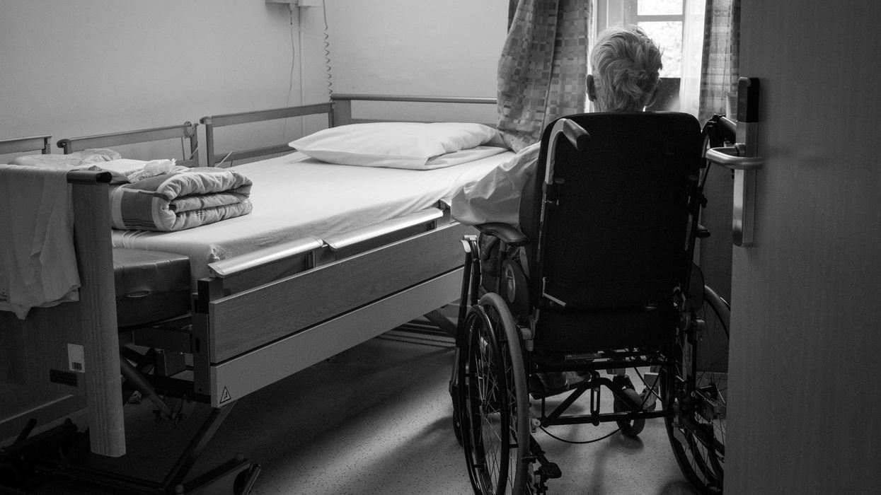 Elderly person in a wheelchair next to an unmade bed