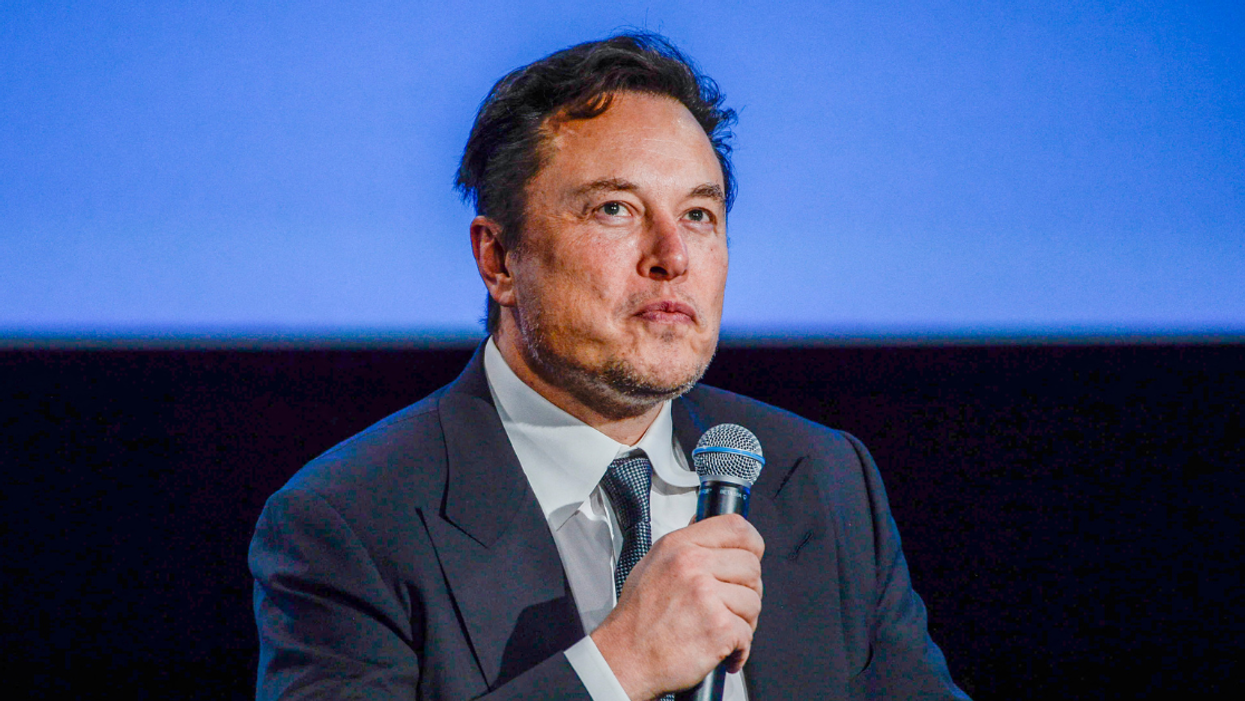 Elon Musk seated and holding a microphone