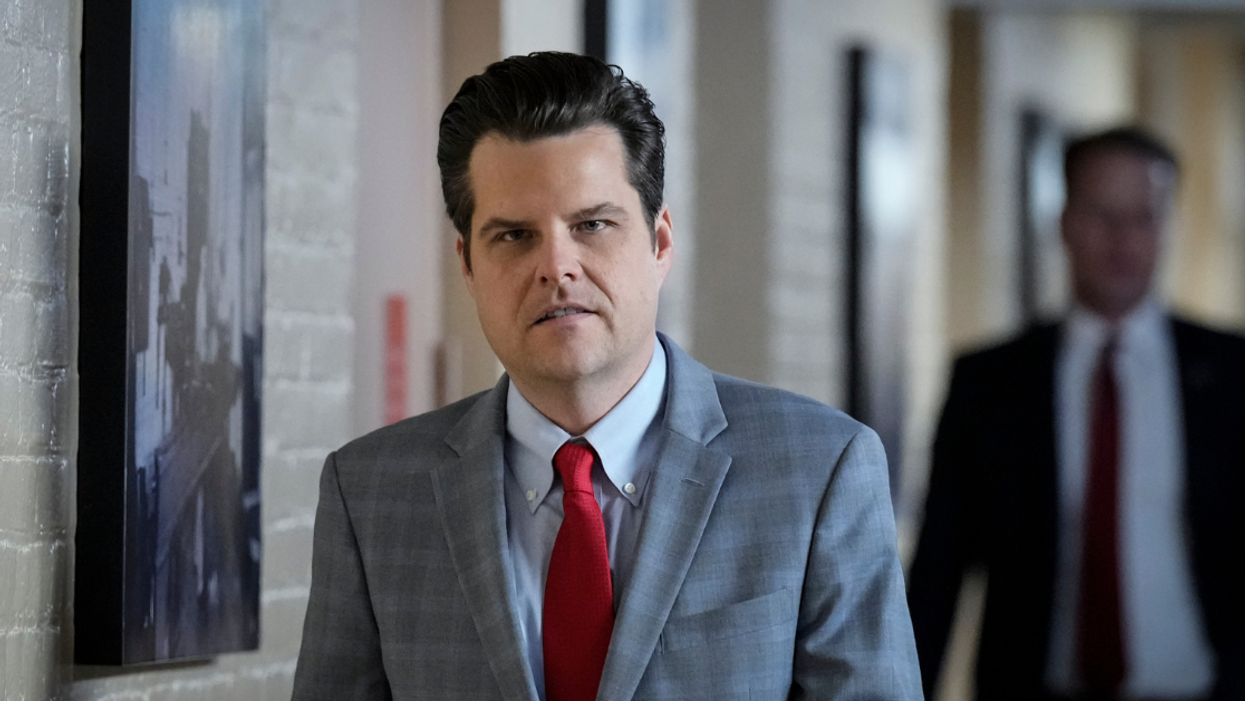 Florida Representative Matt Gaetz walking down a hallway wearing a gray suit and red tie