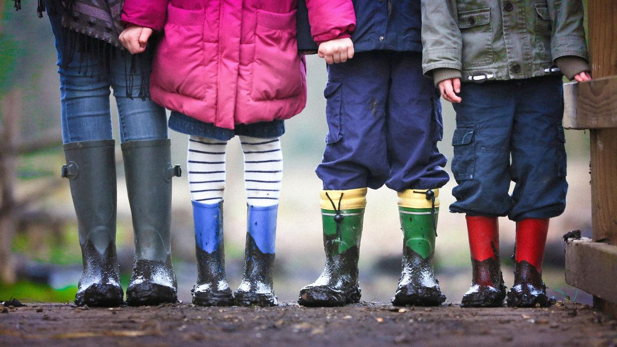 four children in muddy boots standing on dirt during daytime