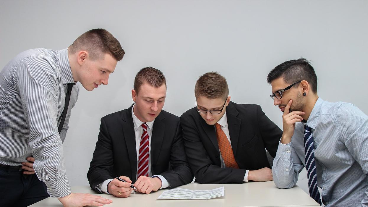 Four men in a boardroom read over a document