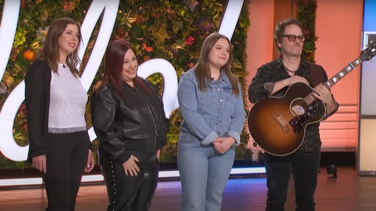 Four people standing together; one holds a guitar.