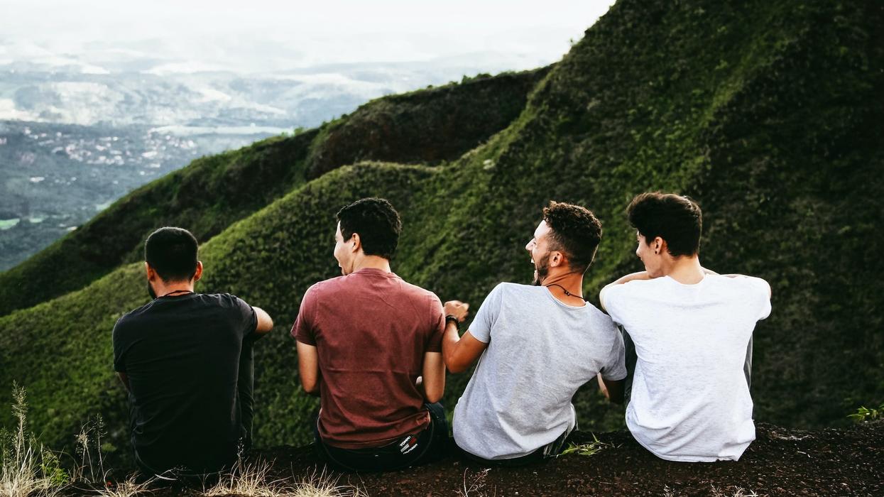 Four young men laugh and talk on a hillside
