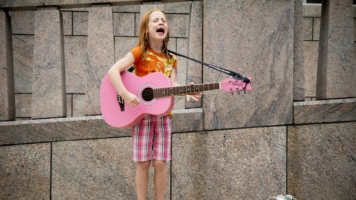 girl busker playing guitar and singing in front of wall