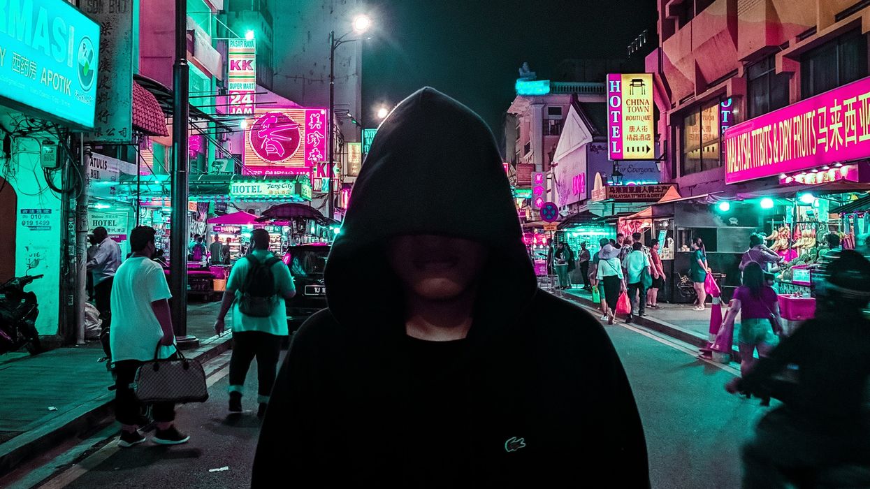 Hooded person walking down busy street at night
