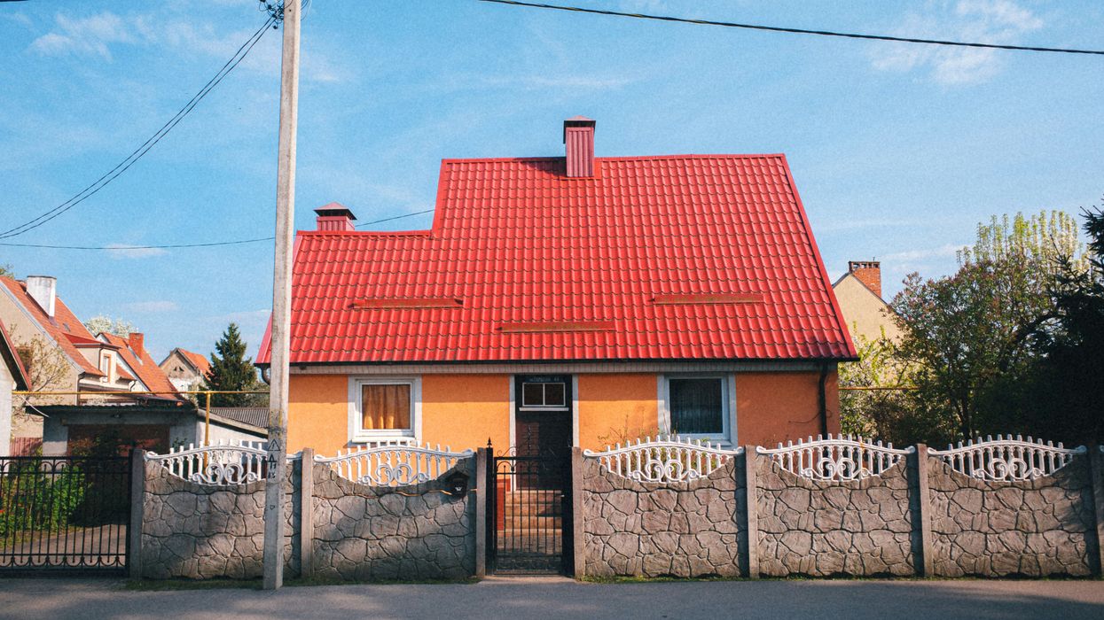 house with orange walls and red roof behind decorative fence