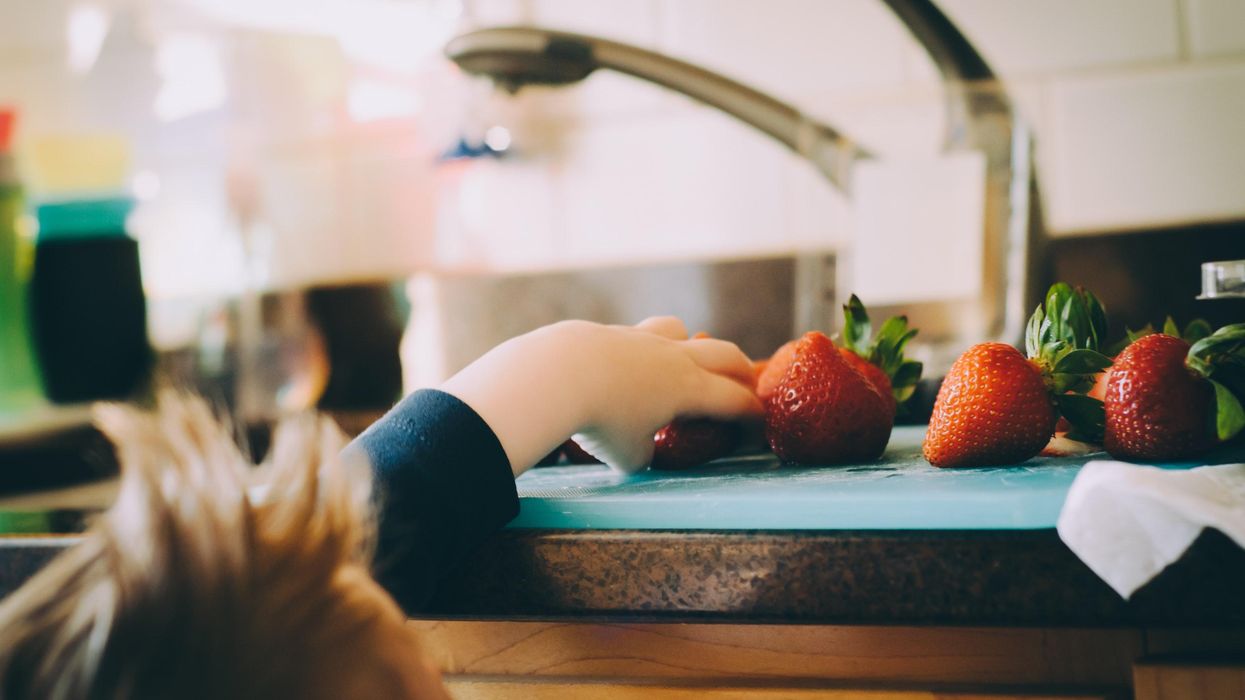 Kid reaching for a strawberry on the kitchen countertop