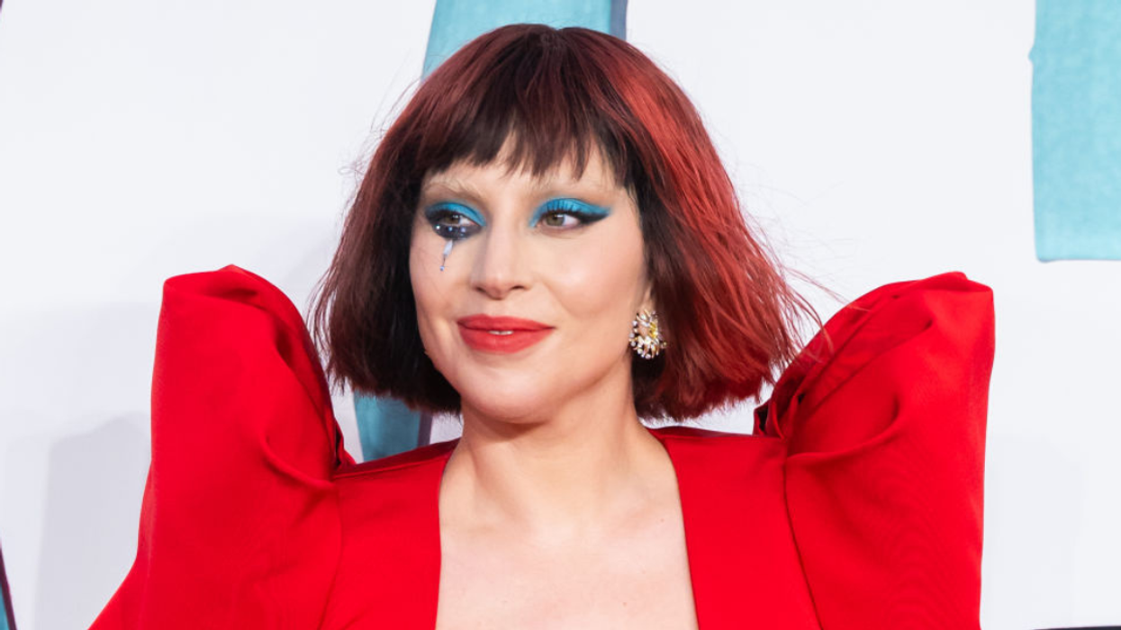 Lady Gaga with red hair wearing a red dress with big sleeves and a made up tear on her cheek.