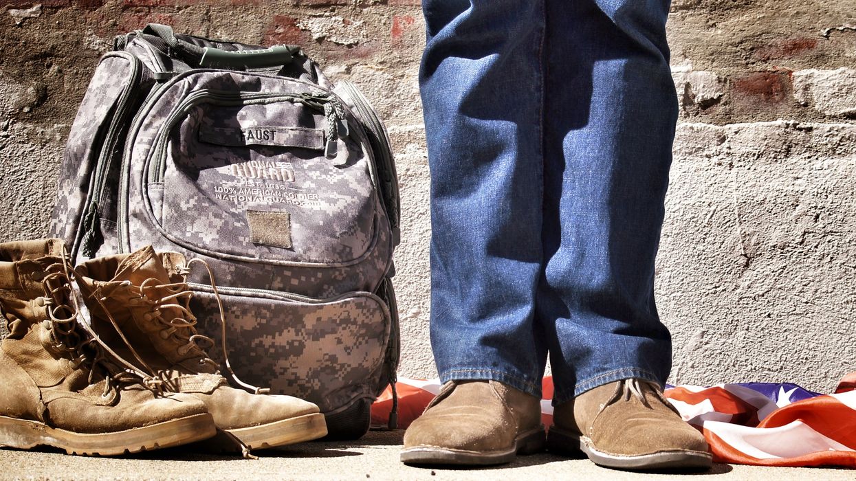 Legs of a Military recruit next to their personal belongings and American flag