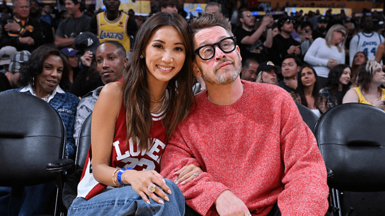 Macaulay Culkin and Brenda Song sitting courtside at a basketball game.