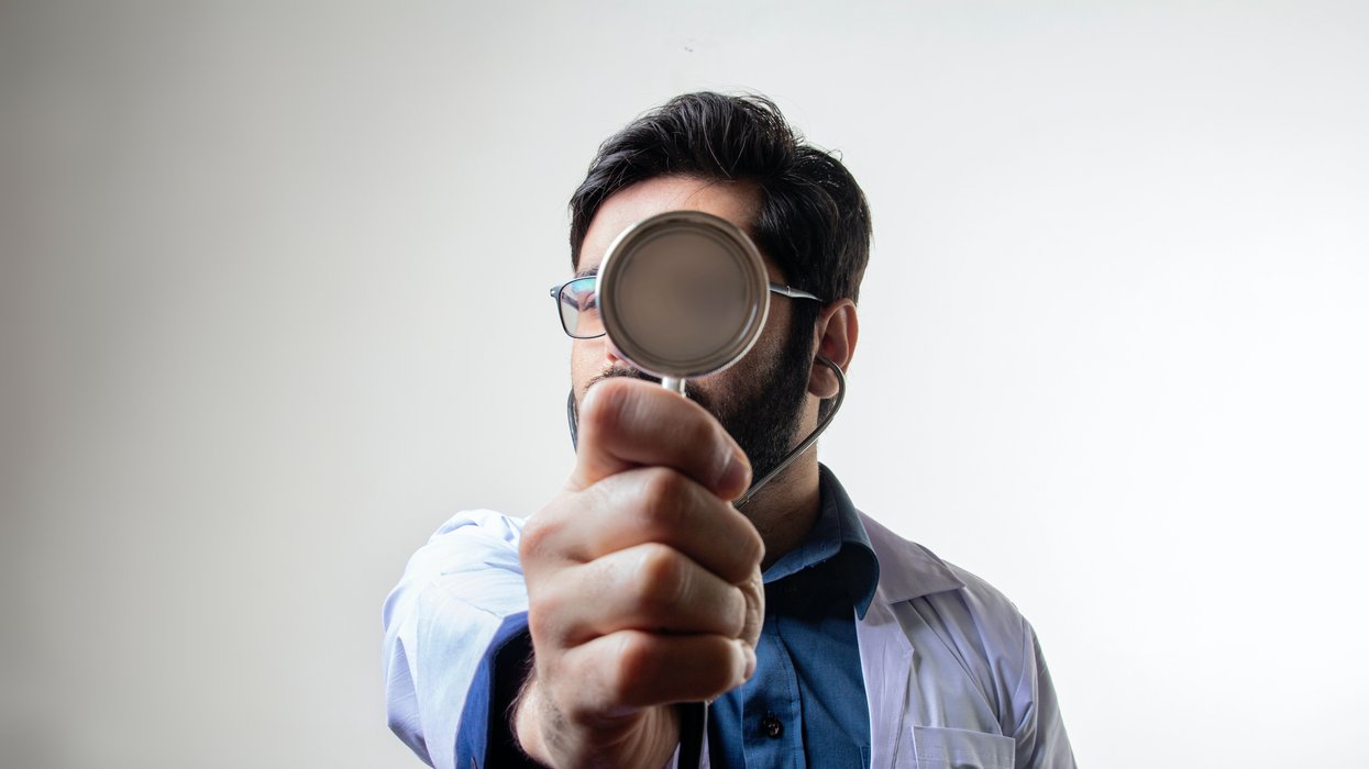 Male doctor holding up stethoscope in front of his face
