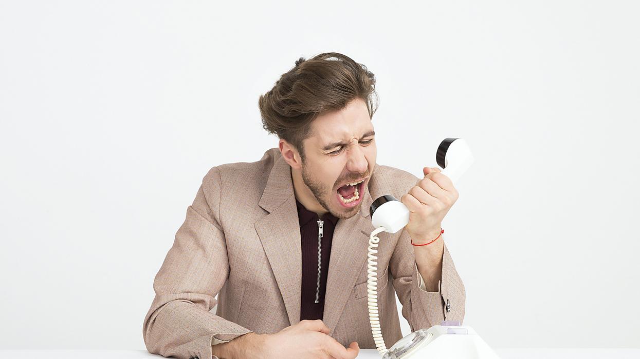man holding telephone screaming into it