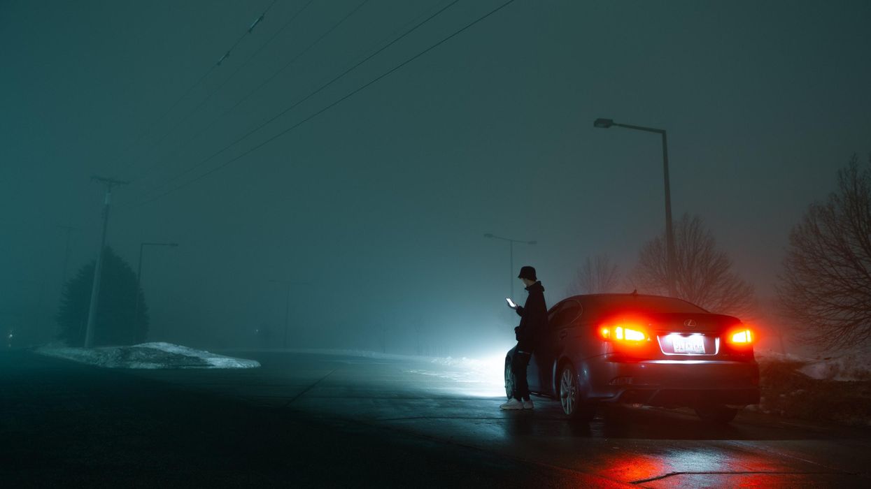 man in black jacket and black pants standing beside red car during night time