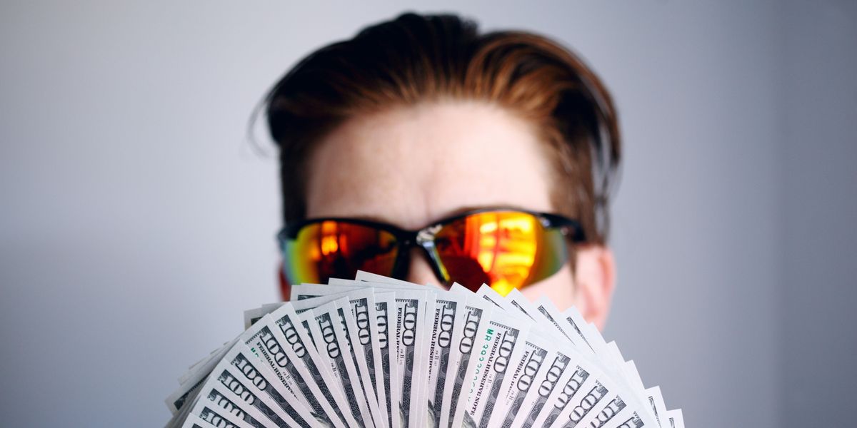 man in sunglasses holding fan of $100 bills