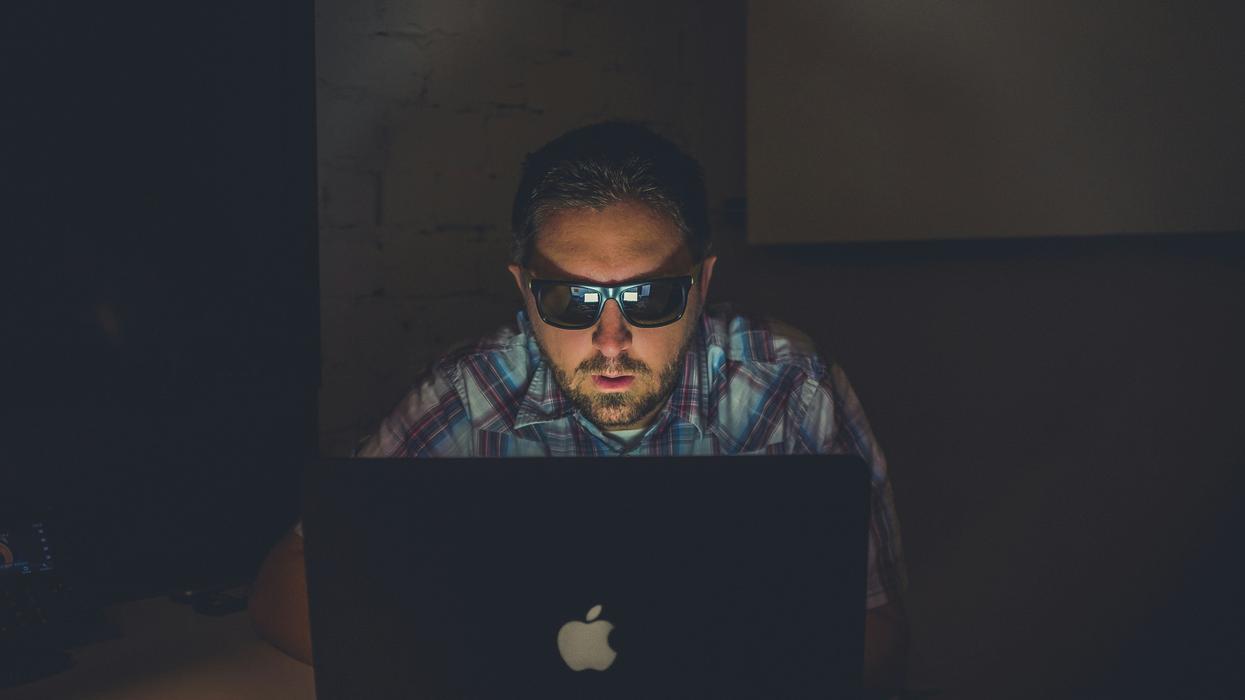 man in sunglasses using laptop in dark room
