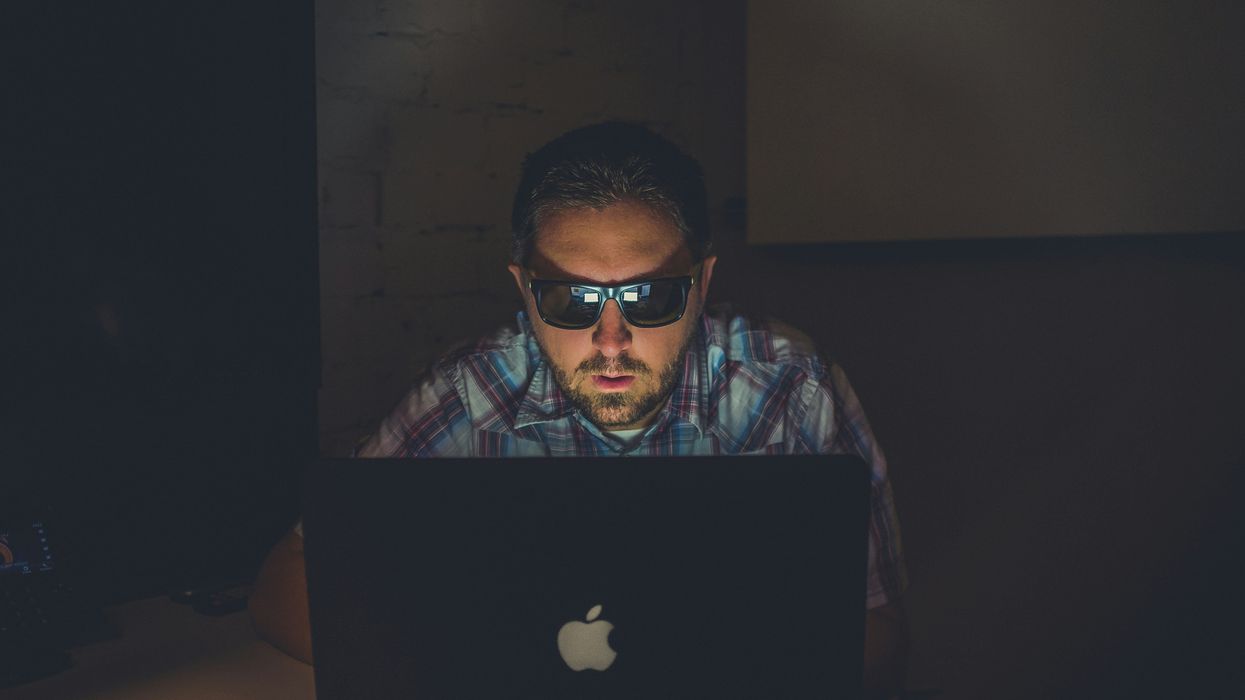 man in sunglasses using laptop in dark room