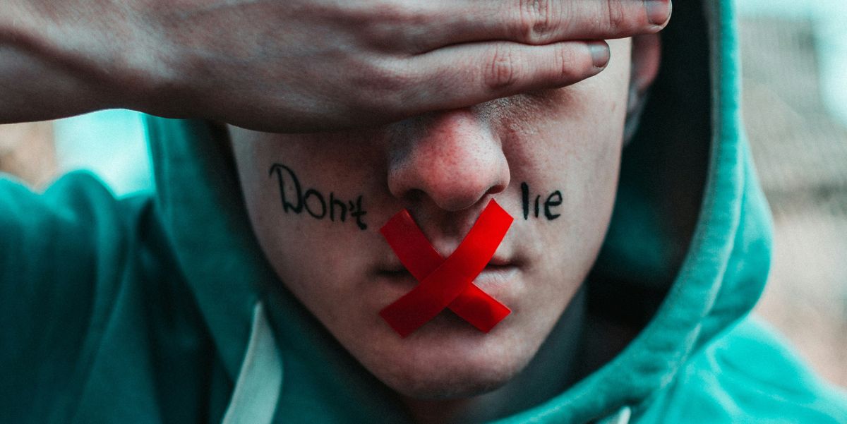 man in teal hoodie with don't lie written on face, red tape on mouth and hand over eyes