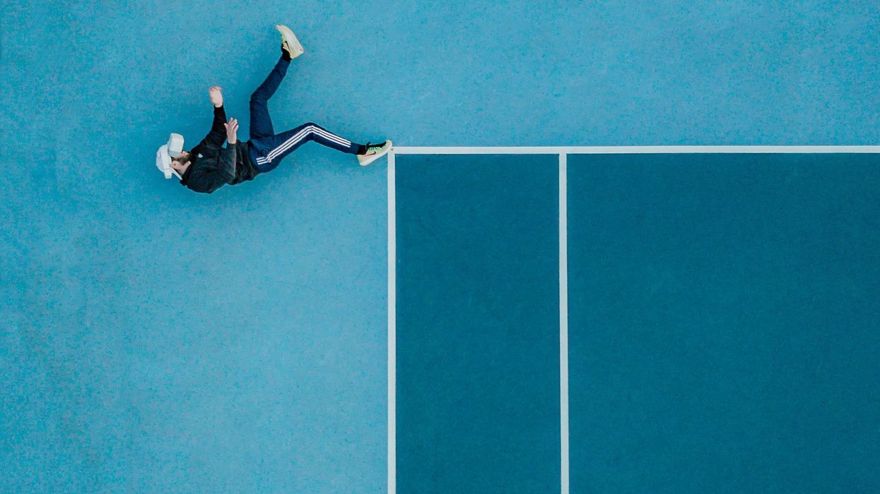 Man lying on edge of tennis court OR man falling off edge of structure
