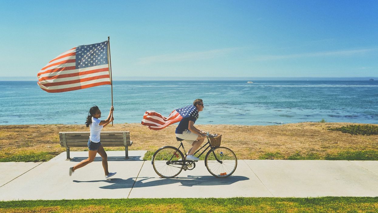 Man on bke wearing an American flag with a woman running behind him holding an American flag.