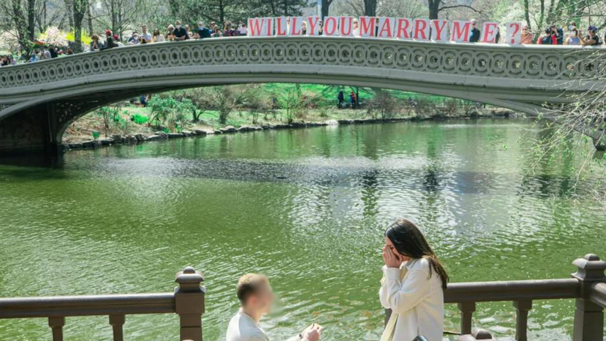 man proposing to woman as people on nearby bridge hold "will you marry me" sign