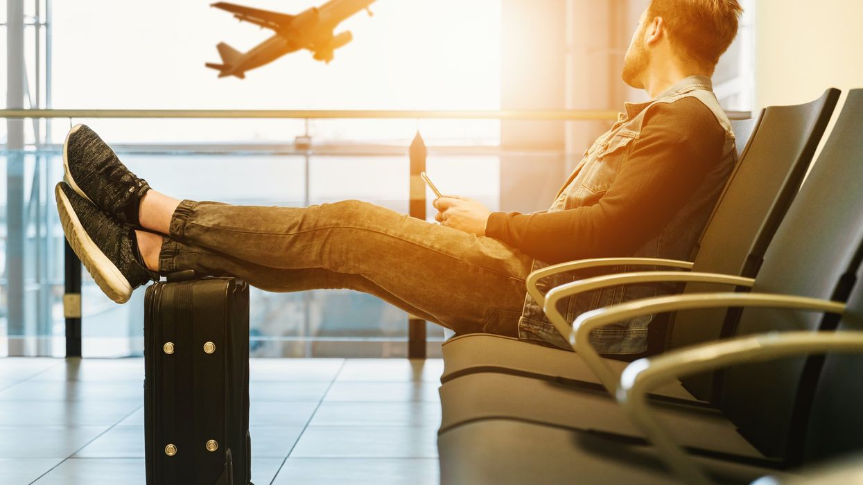 man sitting in airport with feet on luggage looking at airplane