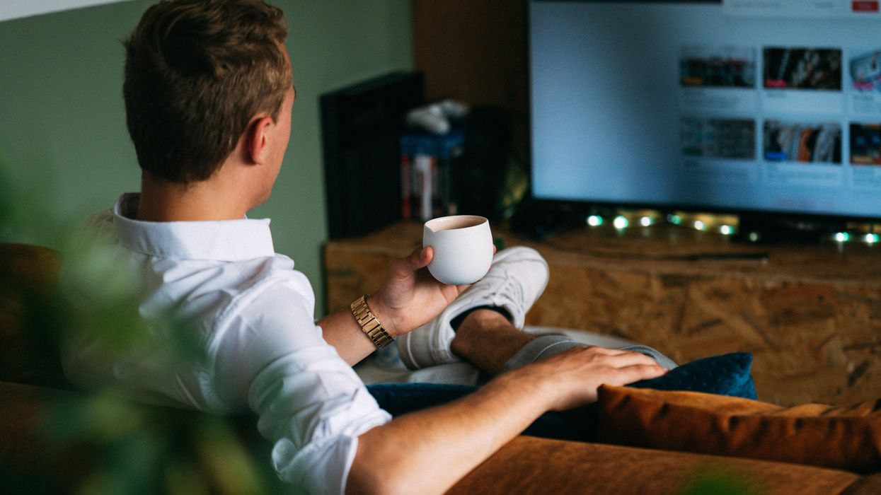 Man sitting on sofa drinking coffee and watching television