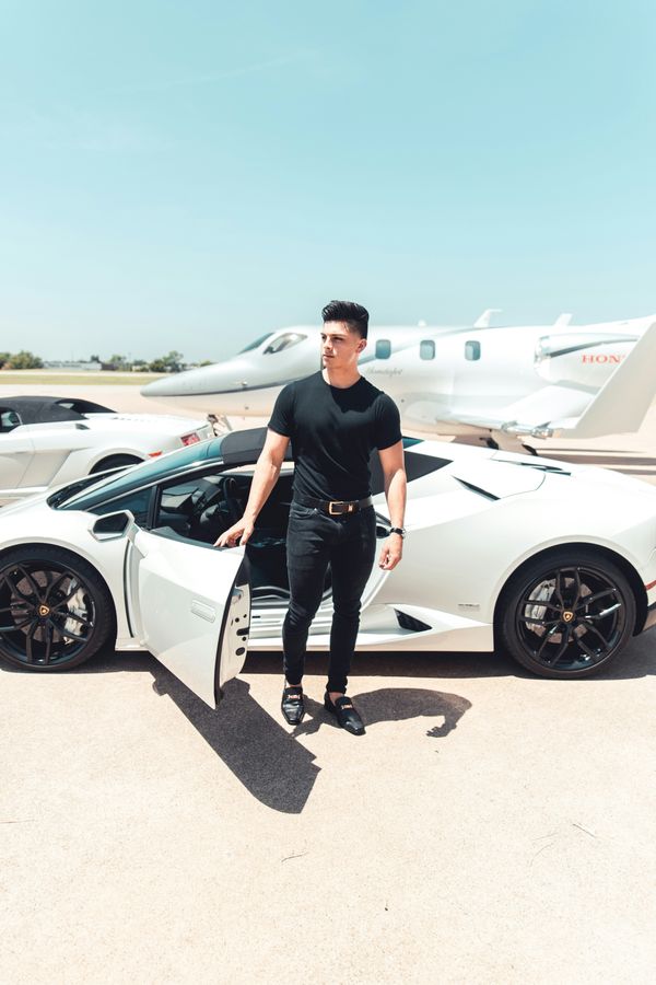 man standing in front of expensive cars and private jet