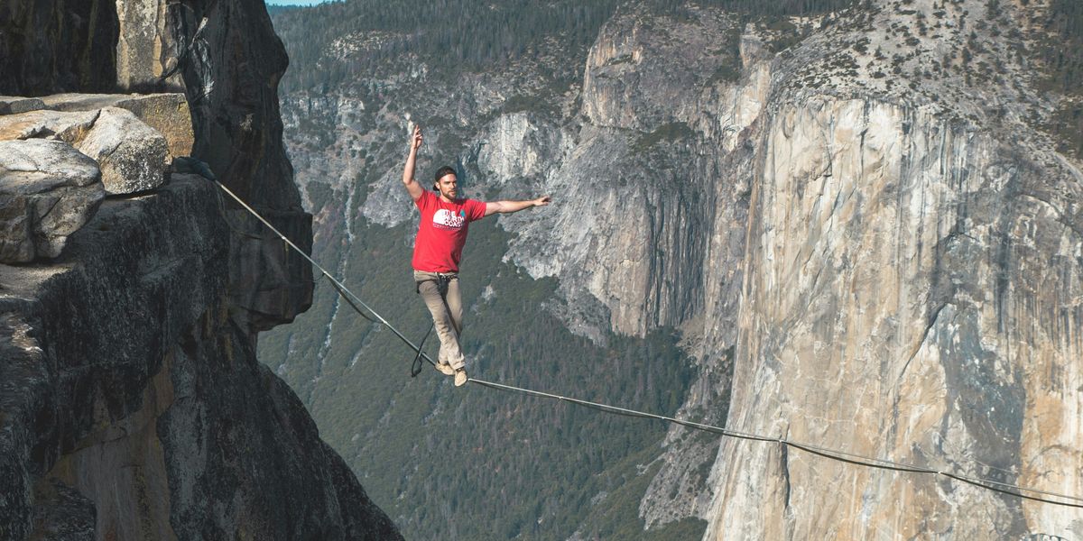 Man walking a tight rope between two cliffs