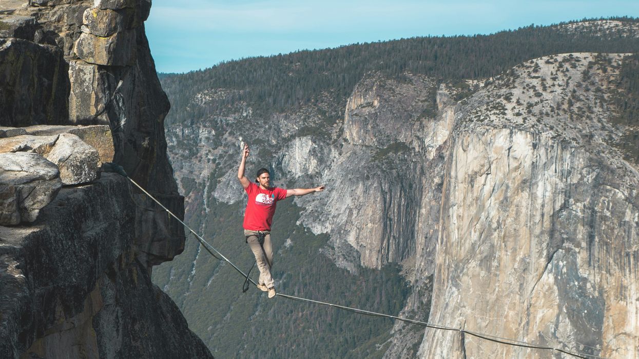 Man walking a tight rope between two cliffs