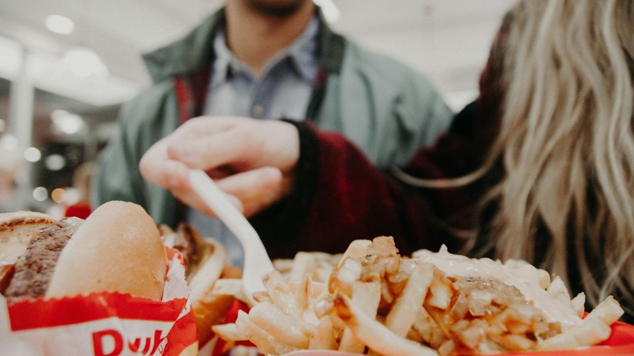 man with woman in maroon long-sleeved shirt holding fork over fries and burger on tray