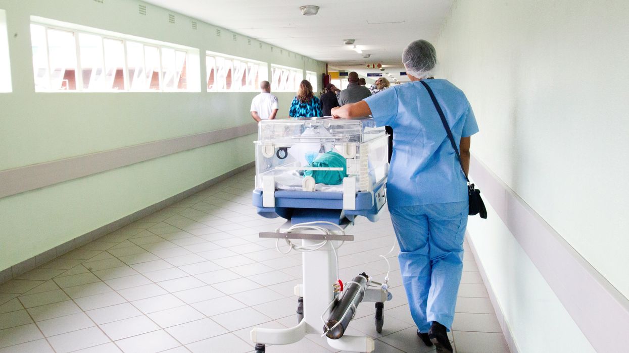 Medical staff member walking down hallway with incubator