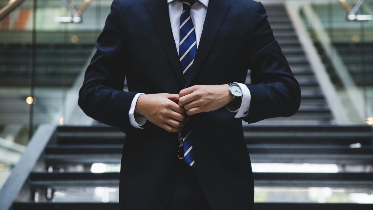 Mid-section shot of a well dressed man buttoning his jacket. He stands on a staircase.